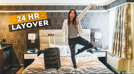 Brunette woman standing on bed in hotel room with suitcase