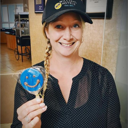 Blonde woman holding up blue smiley face lollipop