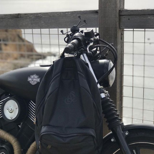 Black backpack hanging from motorcycle parked on coast
