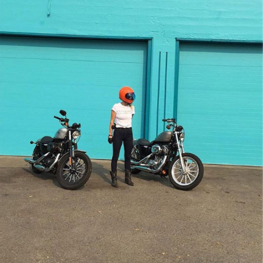 Man with orange helmet between two motorcycles in front of teal wall