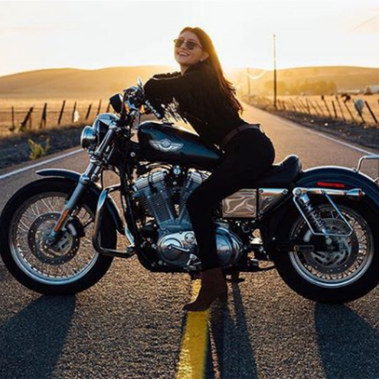 Girl in sunglasses sitting on motorcycle at sunset