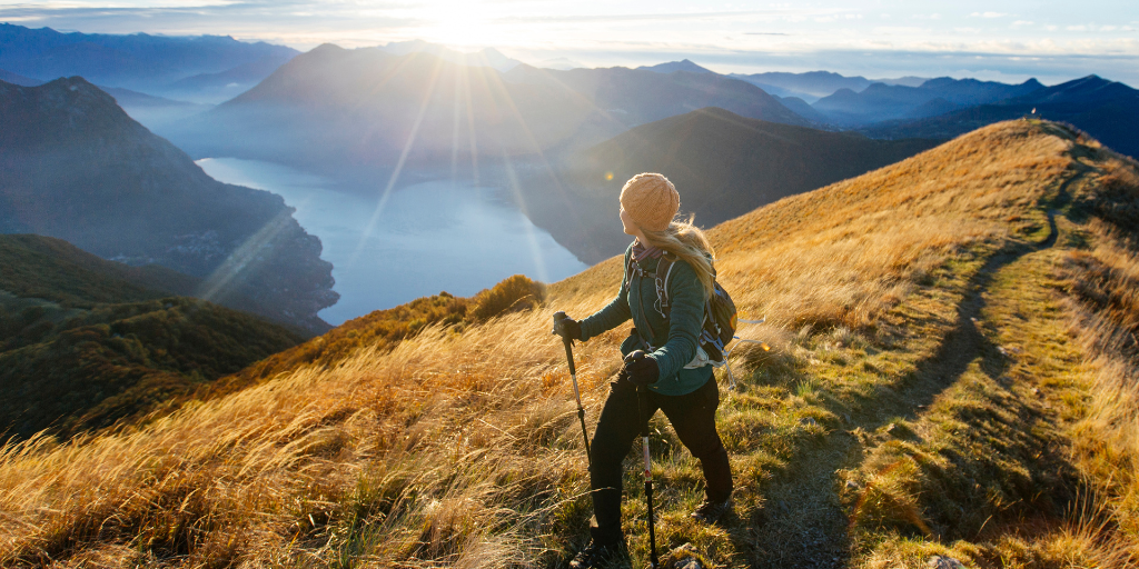 female hiker looks over a beautiful scene with mountains, water, and sunset