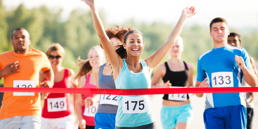female runner crossing a finish line surrounded by a group of diverse runners