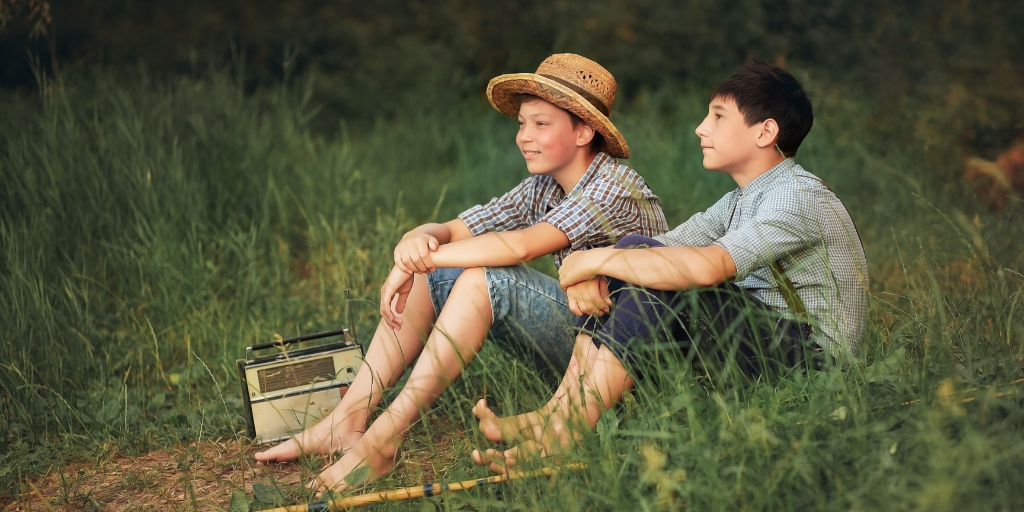 Two boys resembling Tom Sawyer sit in a field of grass