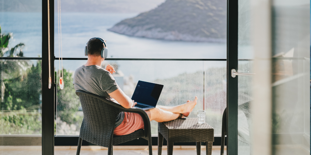Man working on a laptop while sitting in a hotel room overlooking a beautiful body of water
