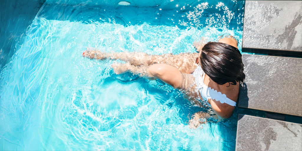Woman sits at the edge of a crystal clear blue pool