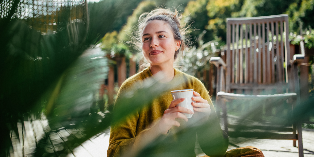 Woman with blonde hair sits on a calm patio drinking coffee