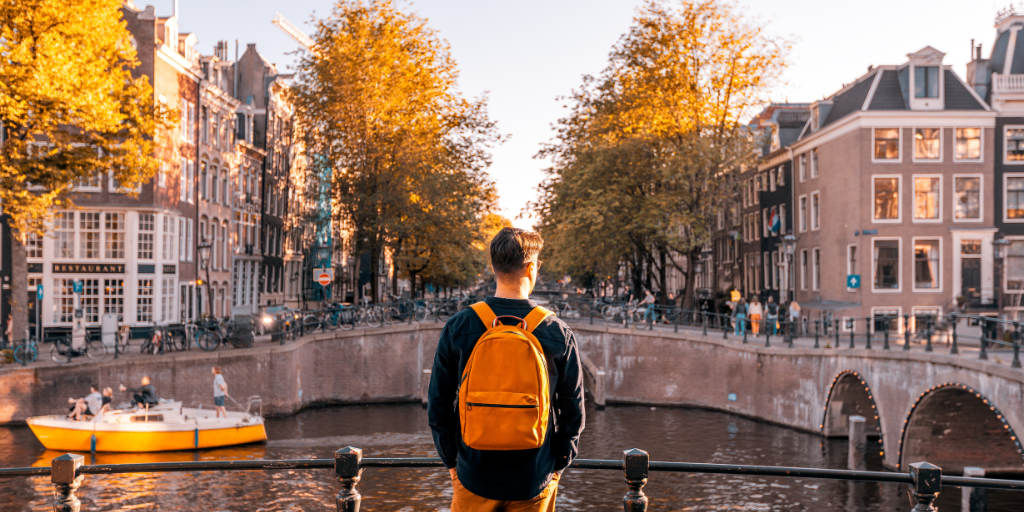 Man with backpack stands in Amsterdam with bright yellow trees