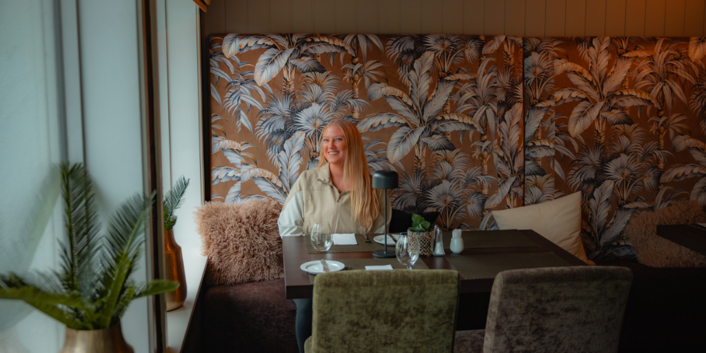 a woman sits in a hotel restaurant with a dynamic wall design behind her
