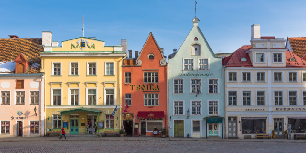 Colorful historic buildings with ornate gabled rooftops line a cobblestone town square beneath a clear blue sky.